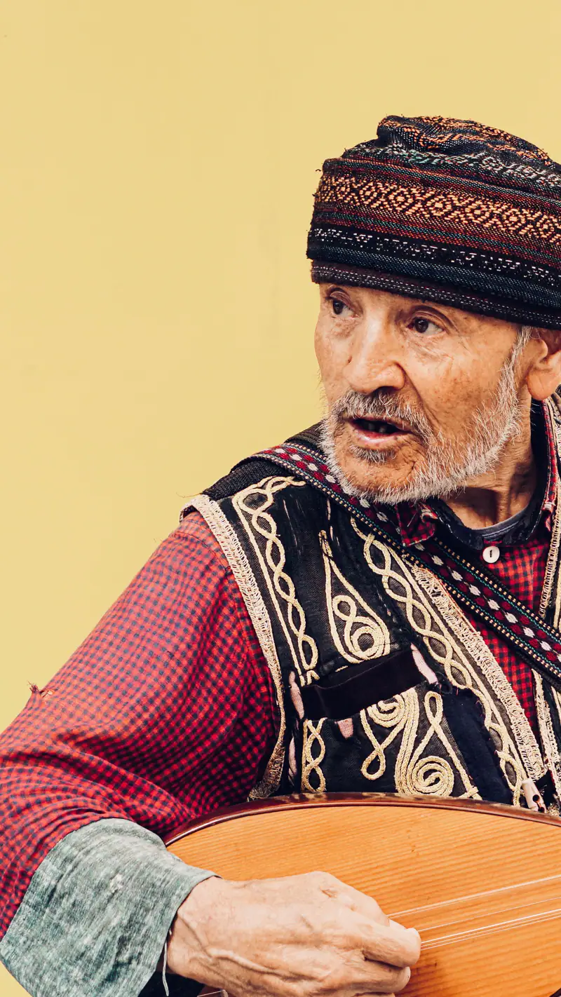 An older musician in a traditional cap with a stringed instrument